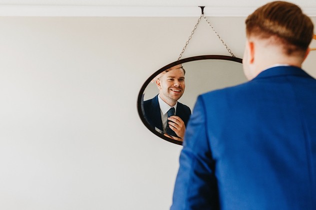 Groom straightening tie in mirror