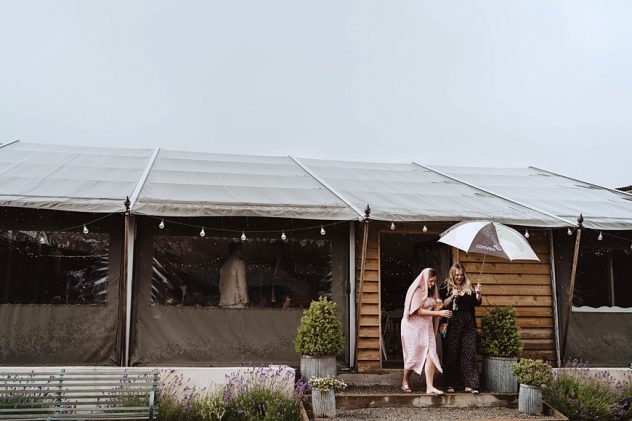 Two wedding guests stepping out of the Wilde Lodge safari tent holding an umbrella