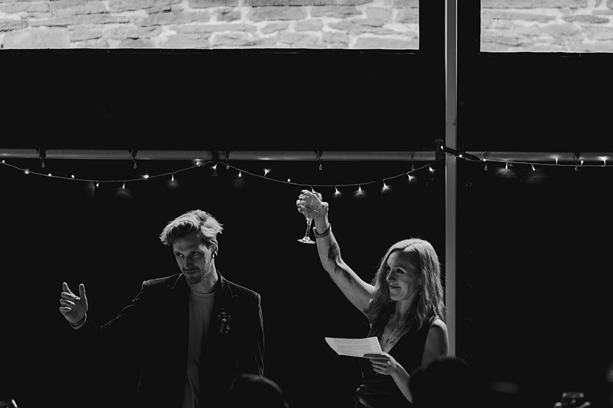 Black and white image of bride and groom raising a toast to guests at Wilde Lodge wedding reception