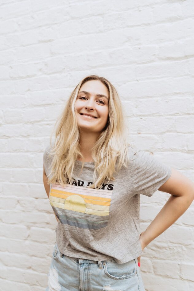 Woman with blonde hair smiles to camera with hands on hips. Business portrait for brand storytelling