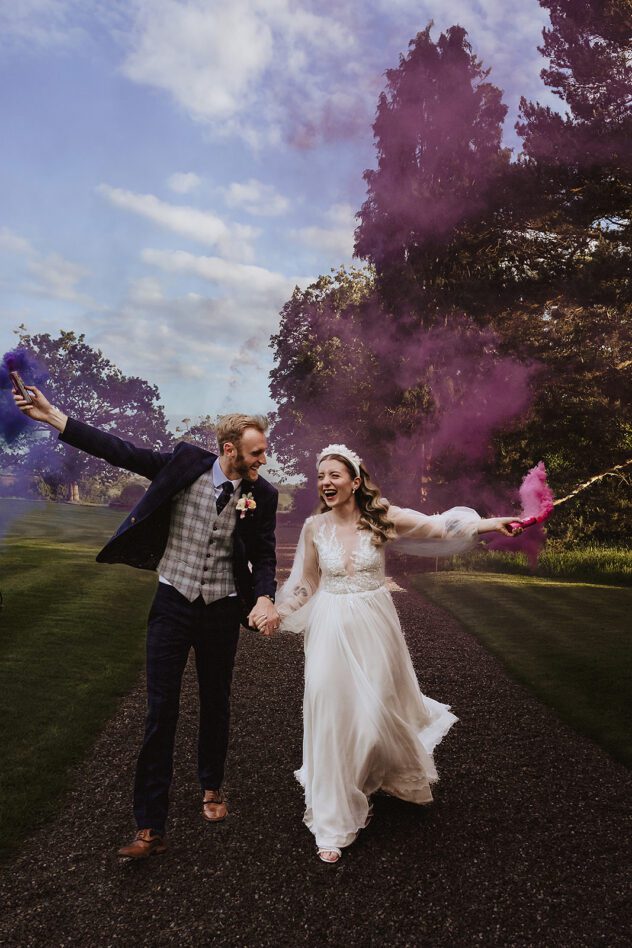 Bride and groom walking with purple and blue smoke bombs Davenport House