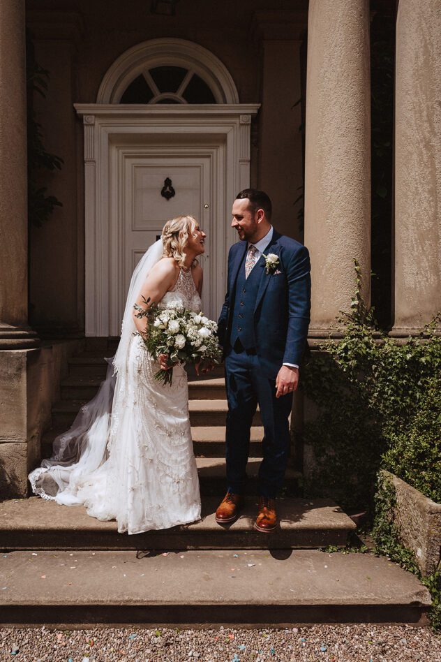 Bride and Groom smiling at each other on the steps outside Iscoyd Park