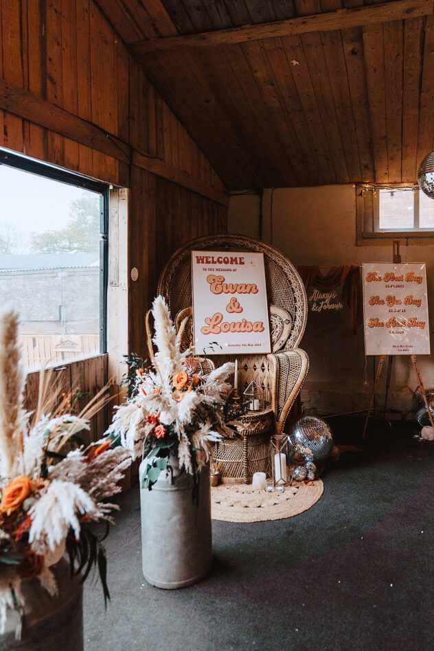 A peacock chair with a disco style wedding sign on it. Urns filled with boho bush flower arrangements at Stanford Farm