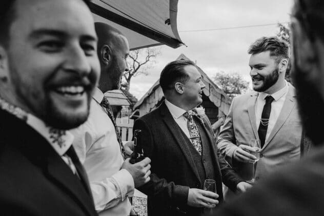 Black and white candid image of groom laughing with guests at Stanford Farm weddin