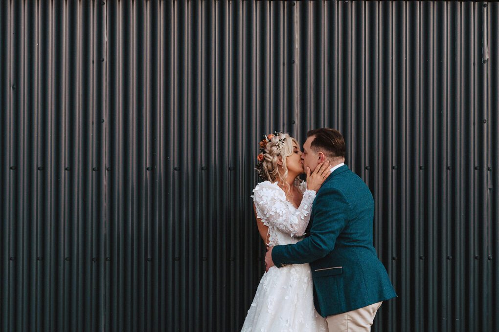 Bride and groom kiss in front of black corrugated iron wall at Stanford Farm Wedding