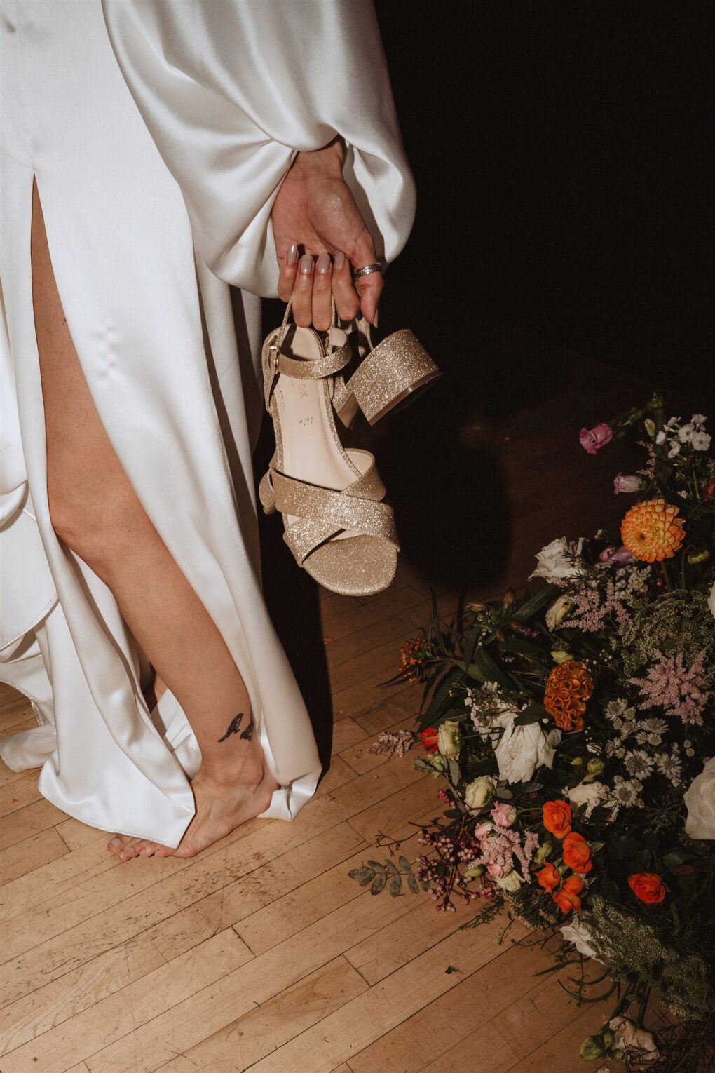 Barefoot bride holding gold sparkly shoes