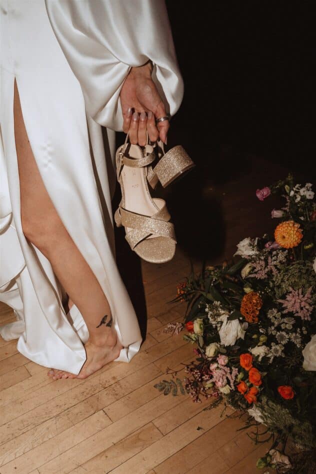 Barefoot bride holding gold sparkly shoes