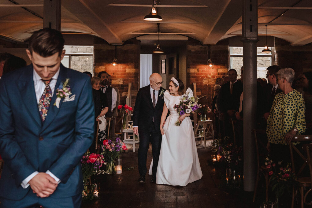 Groom waits at end of aisle as bride walks with father