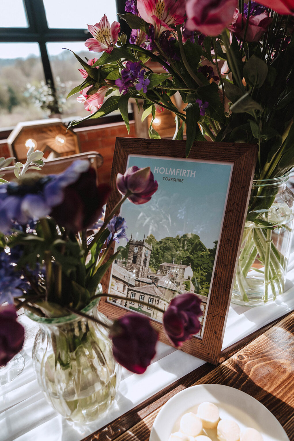 A vase of purple tulips, their heads bowing in front of a Holmfirth Yorkshire poster